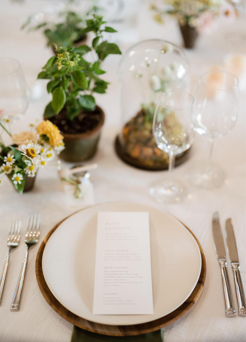 A placesetting at a cottagecore wedding, with moss and a mix of flowers and herbs as part of the display, a matte white plate, and a wooden charger.