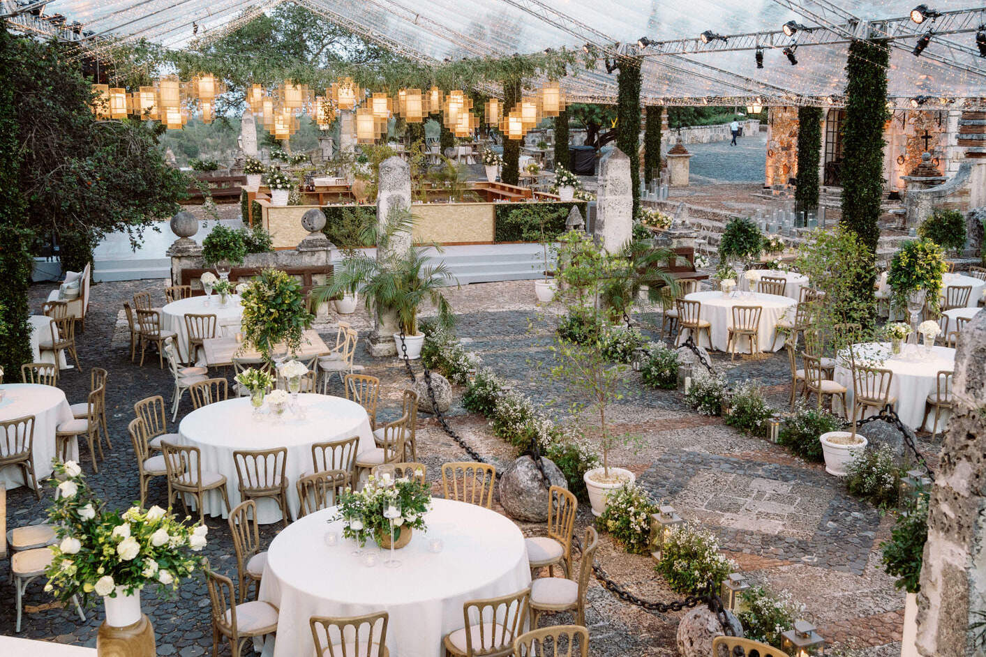 A destination wedding reception is all aglow at dusk, with lighting overhead and candles on the tables.