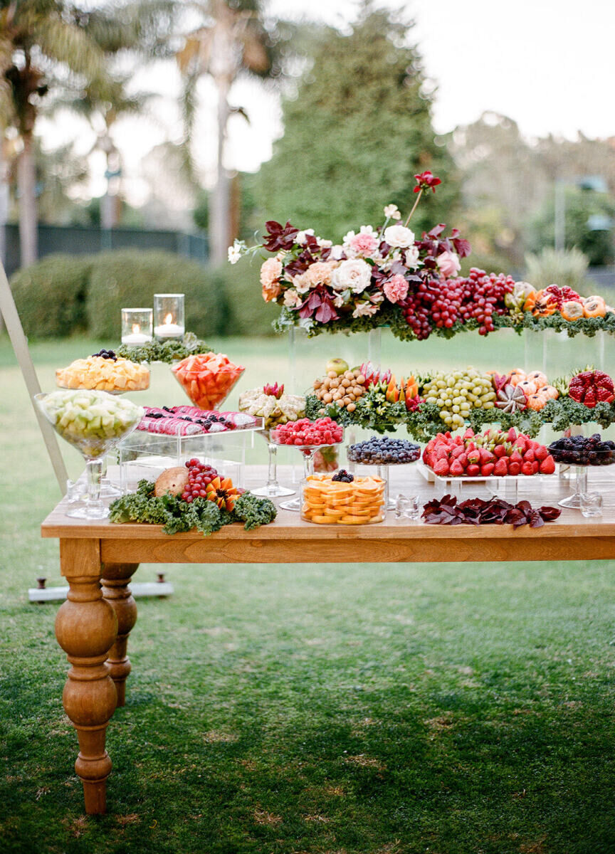 Assorted fruit table, adorned with an earth-toned floral centerpiece next to a tented wedding reception at the Park Hyatt Aviara Resort.