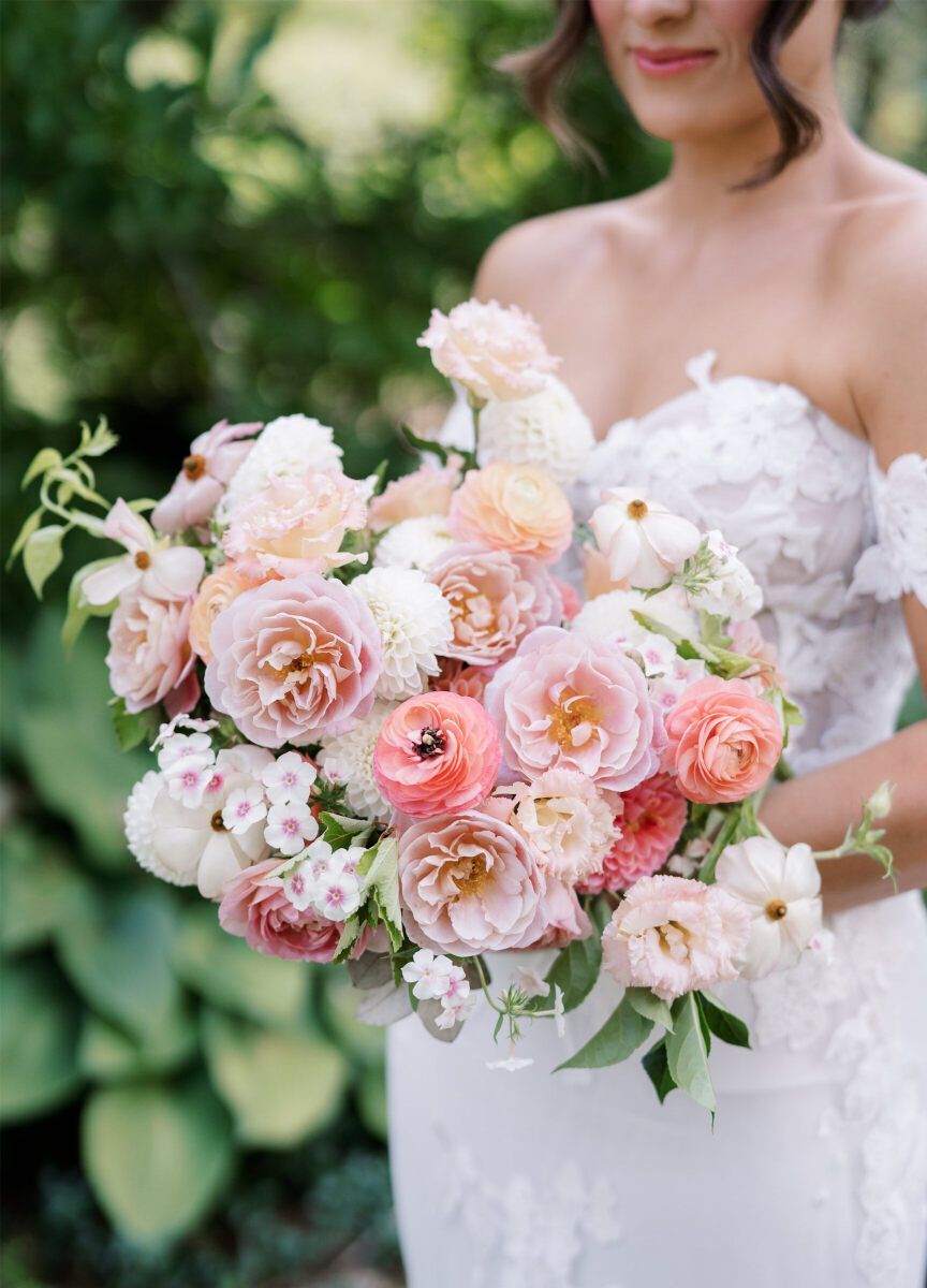 A bride holds her pink, peach, and white bouquet at her enchanted garden wedding.