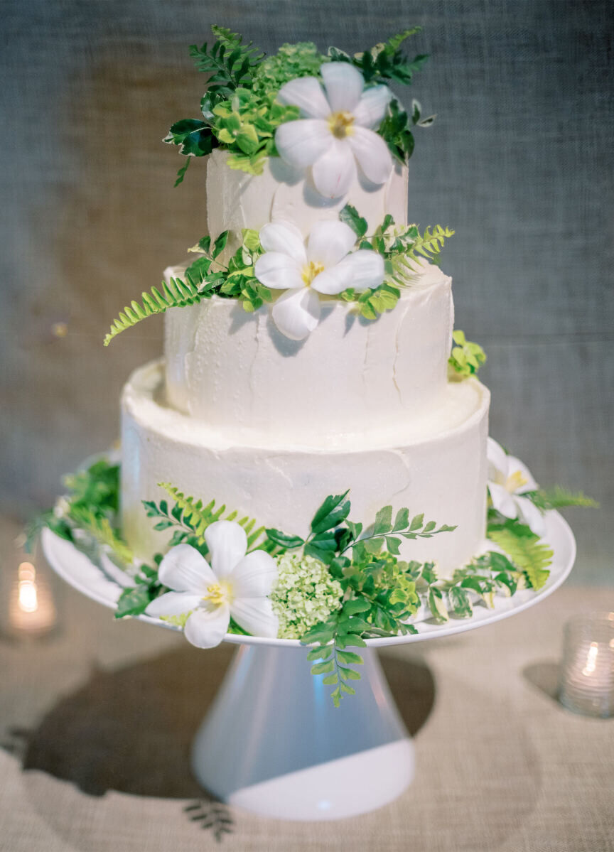 A three-tier cake was covered with buttercream and fresh flowers and ferns at an enchanted waterfront wedding.