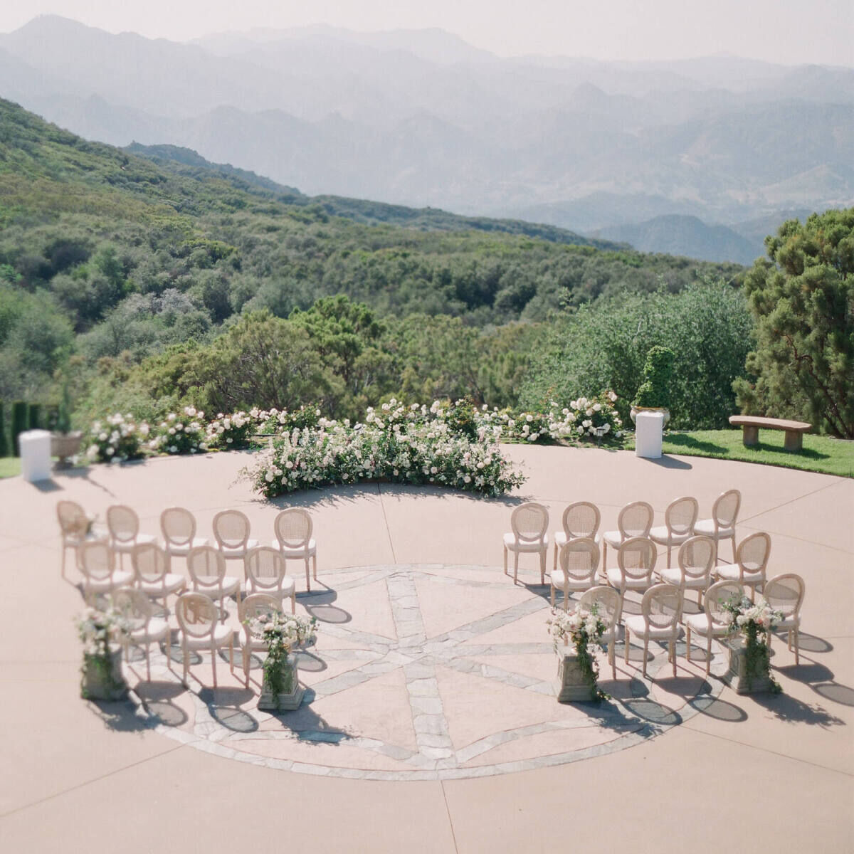 An intimate ceremony set with a low floral arrangement and wood chairs overlooking the hills of Malibu.