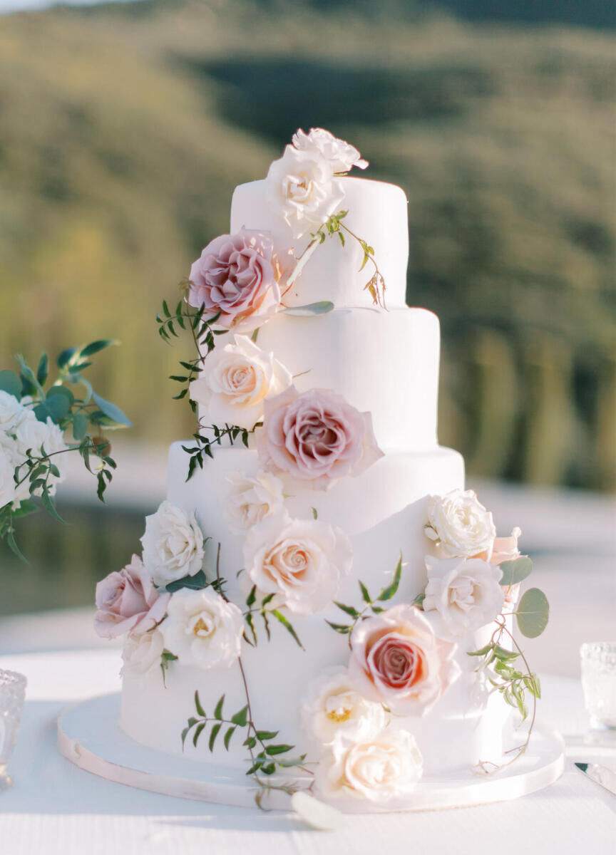 A four-tier wedding cake decorated with fresh roses in shades of white and pink.