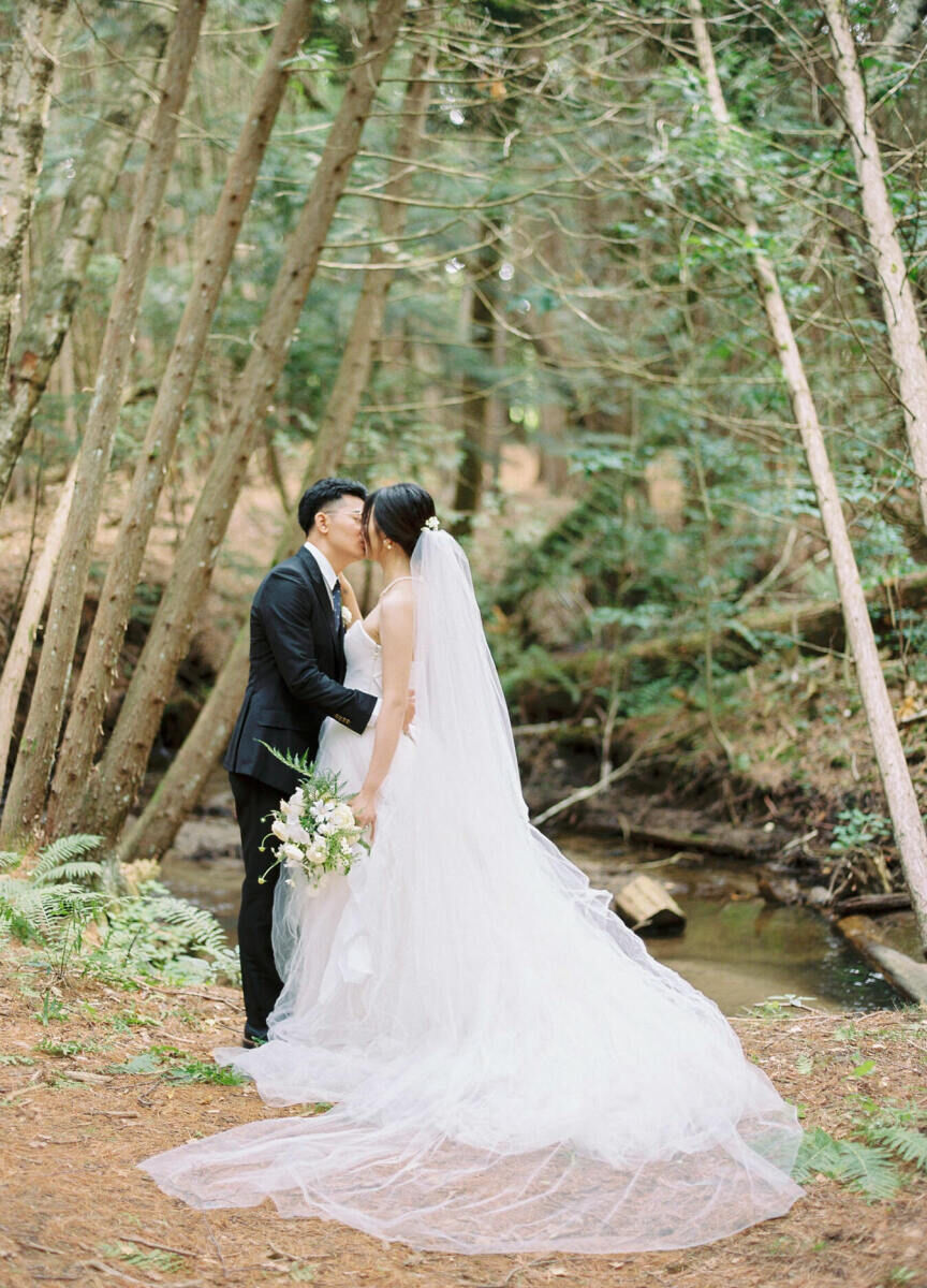 Wedding couple kissing next to a stream at their forest fairytale wedding.