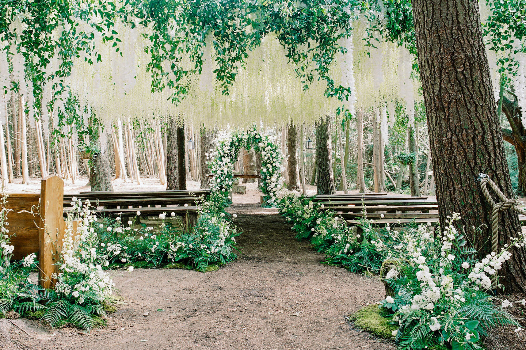 A forest wedding ceremony set-up with a mix of fresh and faux flowers and an abundance of greenery, in an outdoor chapel at a wedding venue in Canada.