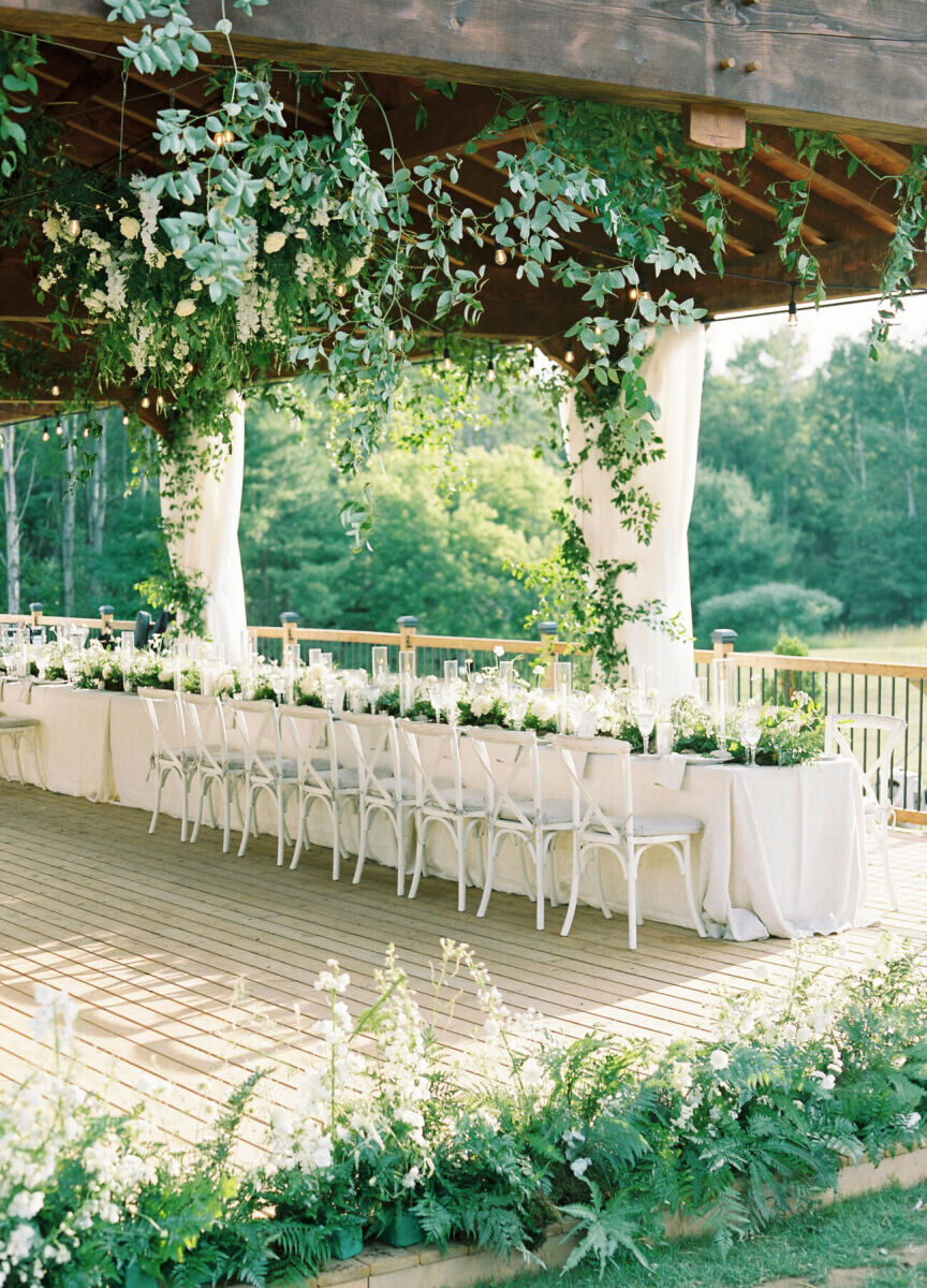 An outdoor reception after a forest wedding ceremony, all decorated in shades of white and green with lots of flowers and fresh greenery.