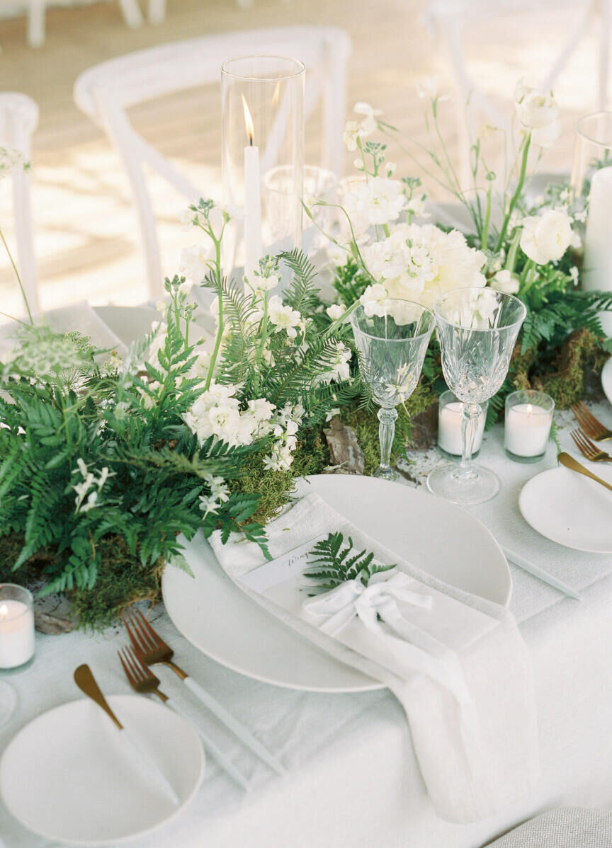 The centerpieces at a forest wedding melded with the setting thanks to fresh ferns and moss, while the tables were made more modern with sleek and simple plates and gold-and-white flatware.