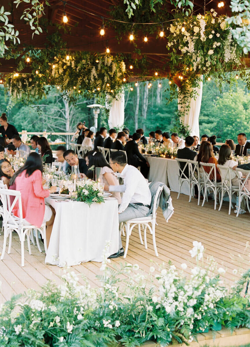 Guests enjoyed an Asian-fusion meal during a forest wedding reception, where bistro bulbs and greenery hung overhead.