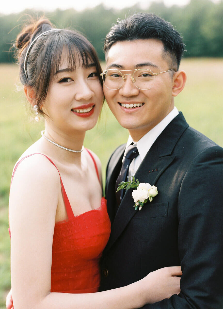 A bride (in a red reception dress) and groom ake a close-up portrait at the Canadian wedding venue where their forest wedding took place.