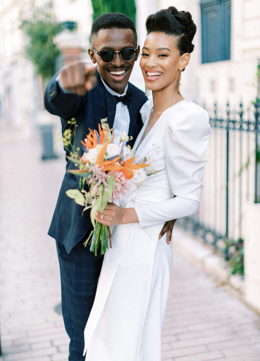 A smiling groom and bride look at the photographer while taking portraits at their French wedding.