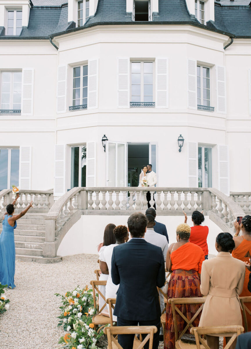 The bride and groom in front of the chateau where their French wedding took place, looking at their guests post-ceremony.