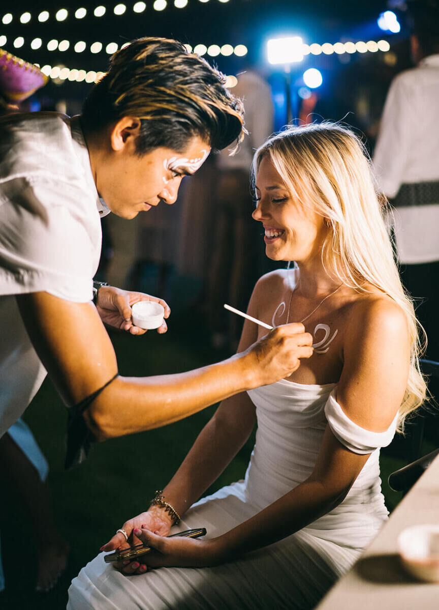 At a glam beach wedding, an artist paints guests with white body paint during the reception.