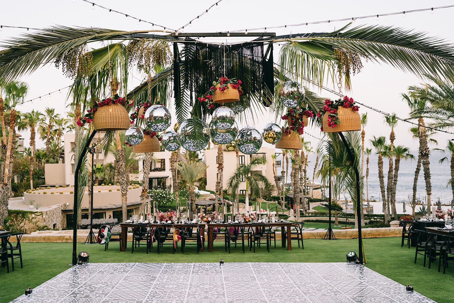 A glam beach wedding reception gave waterfront views and a fun, party vibe, courtesy of disco balls, woven light fixtures, and palm trees over a faux-tile dance floor, surrounded by the tables set for 75 guests.