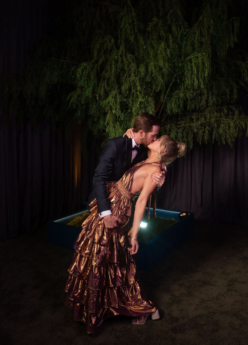 A pair of guests embrace in front of a tree that provided a backdrop for the photo booth at a glam enchanted wedding.