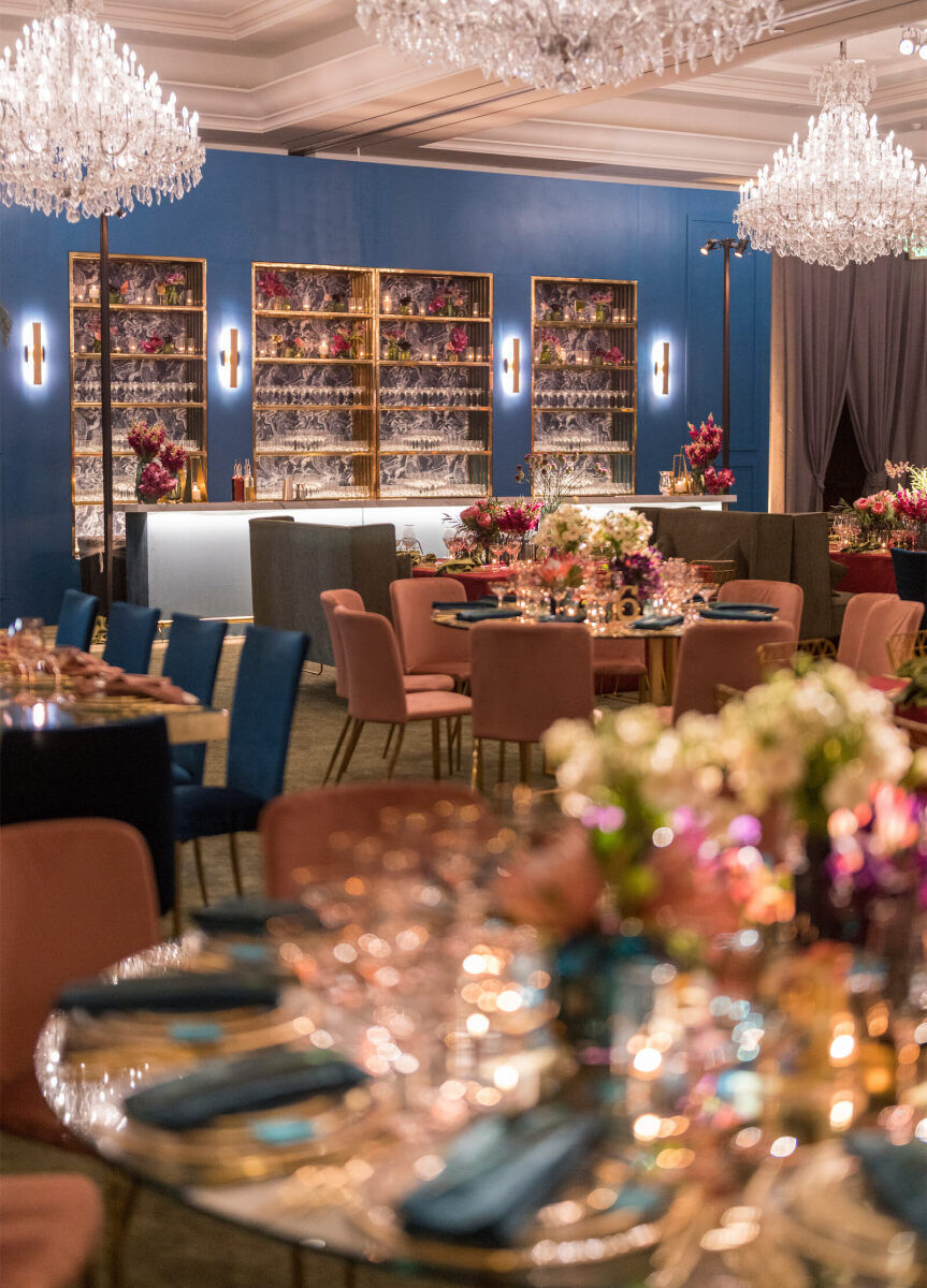 A glam enchanted wedding reception in a ballroom, with a custom bar built on one wall, and a mix of tables dotting the floor.