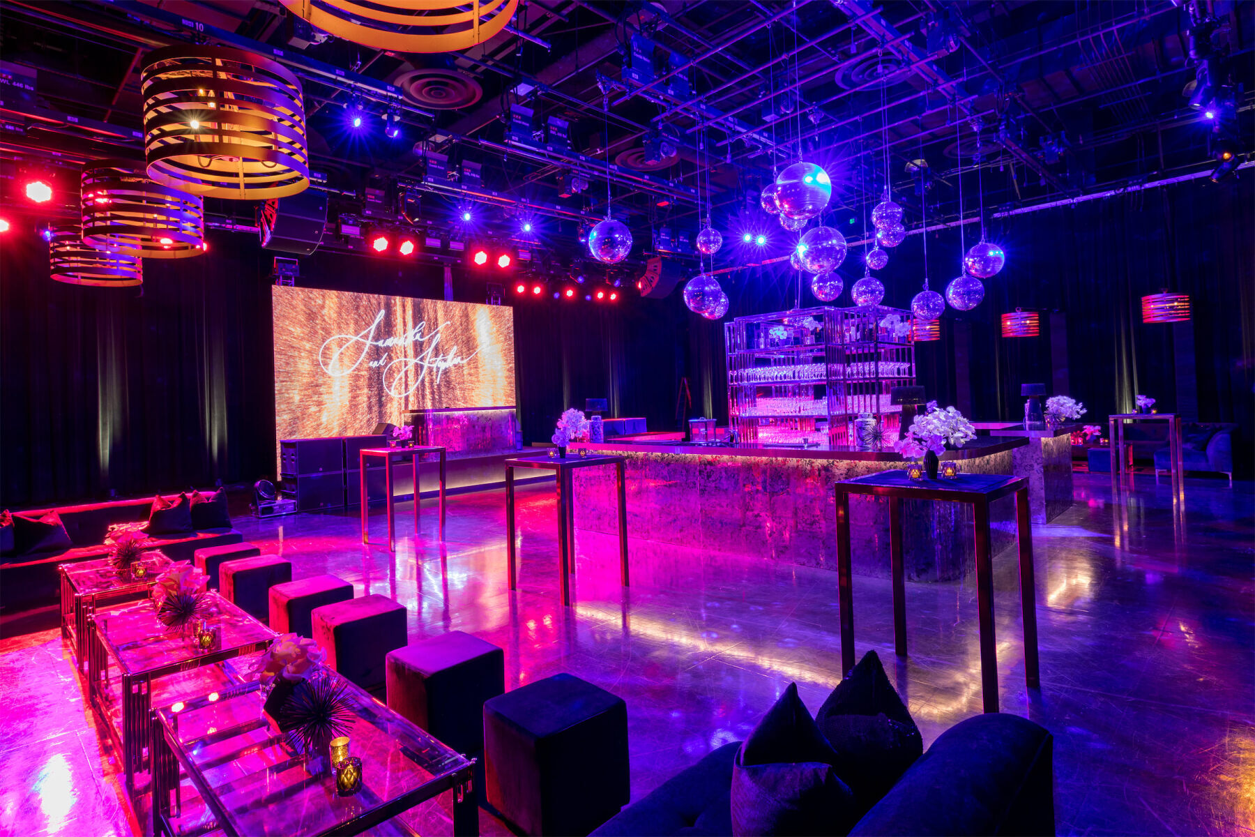 An after-party space in a hotel was transformed for a glam enchanted wedding with colored lighting, disco balls, and the couple's name displayed on a screen.