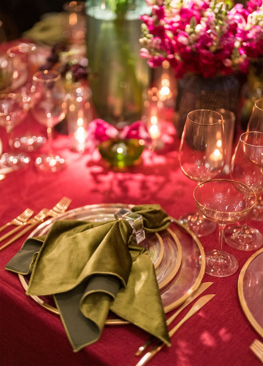 Green velvet napkins popped on gold-rimmed plates atop a pink linen at a glam enchanted wedding reception that was all about color.