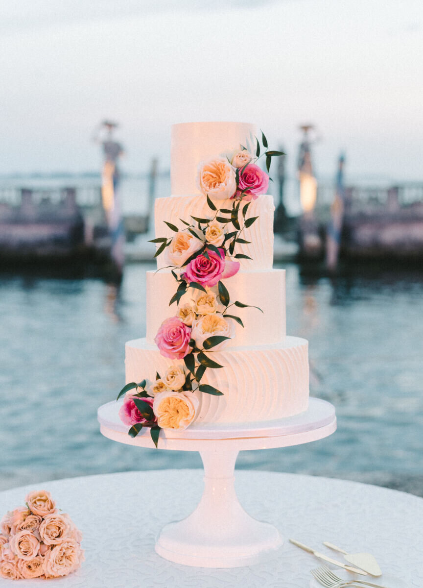 A four-tier wedding cake decorated with a cascade of fresh blooms at a glam, garden wedding reception in Miami.
