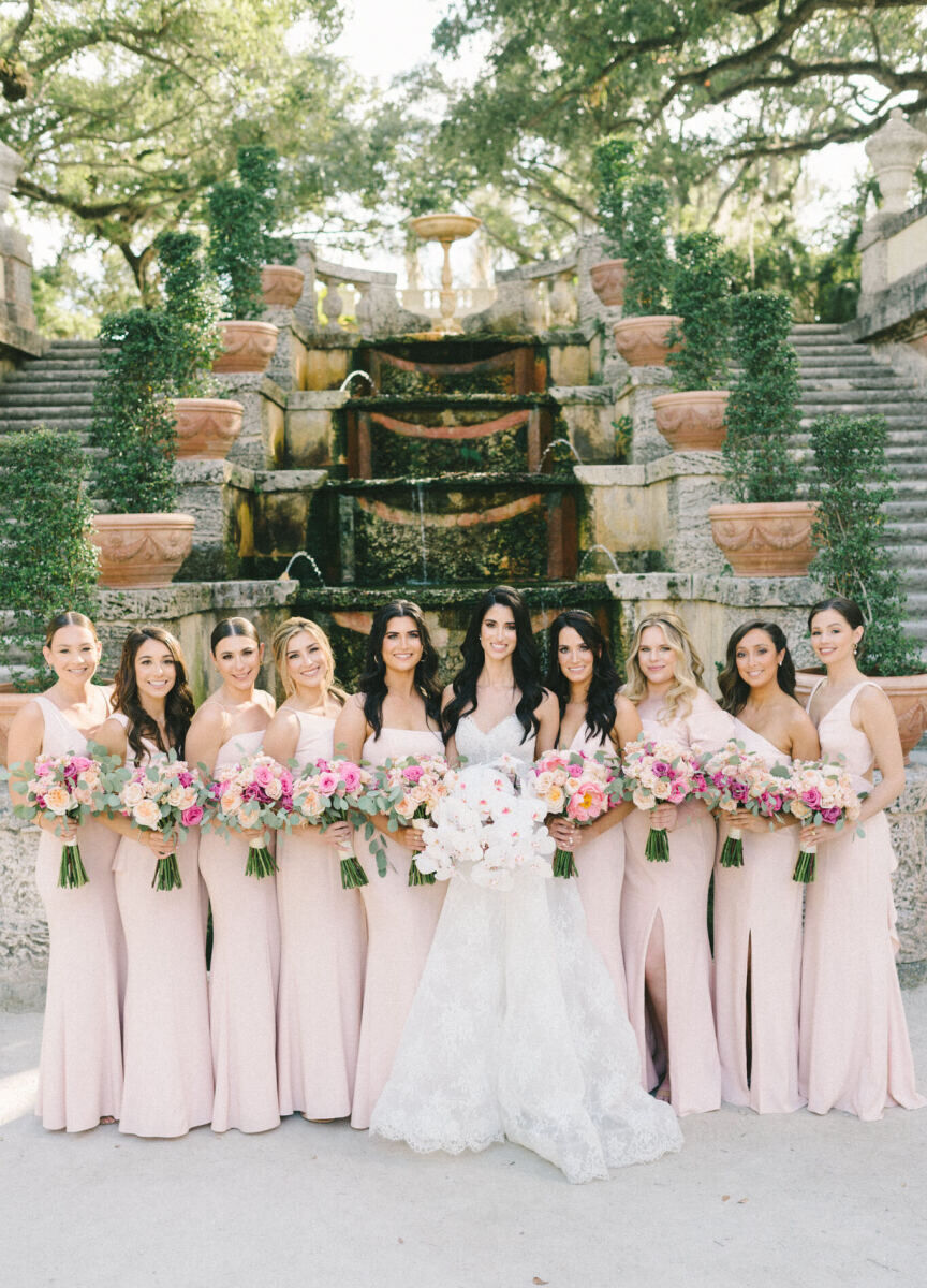 A bride, surrounded by her bridesmaids in pink gowns, hold their bouquets, which they carried down the aisle of this glam, garden wedding ceremony.