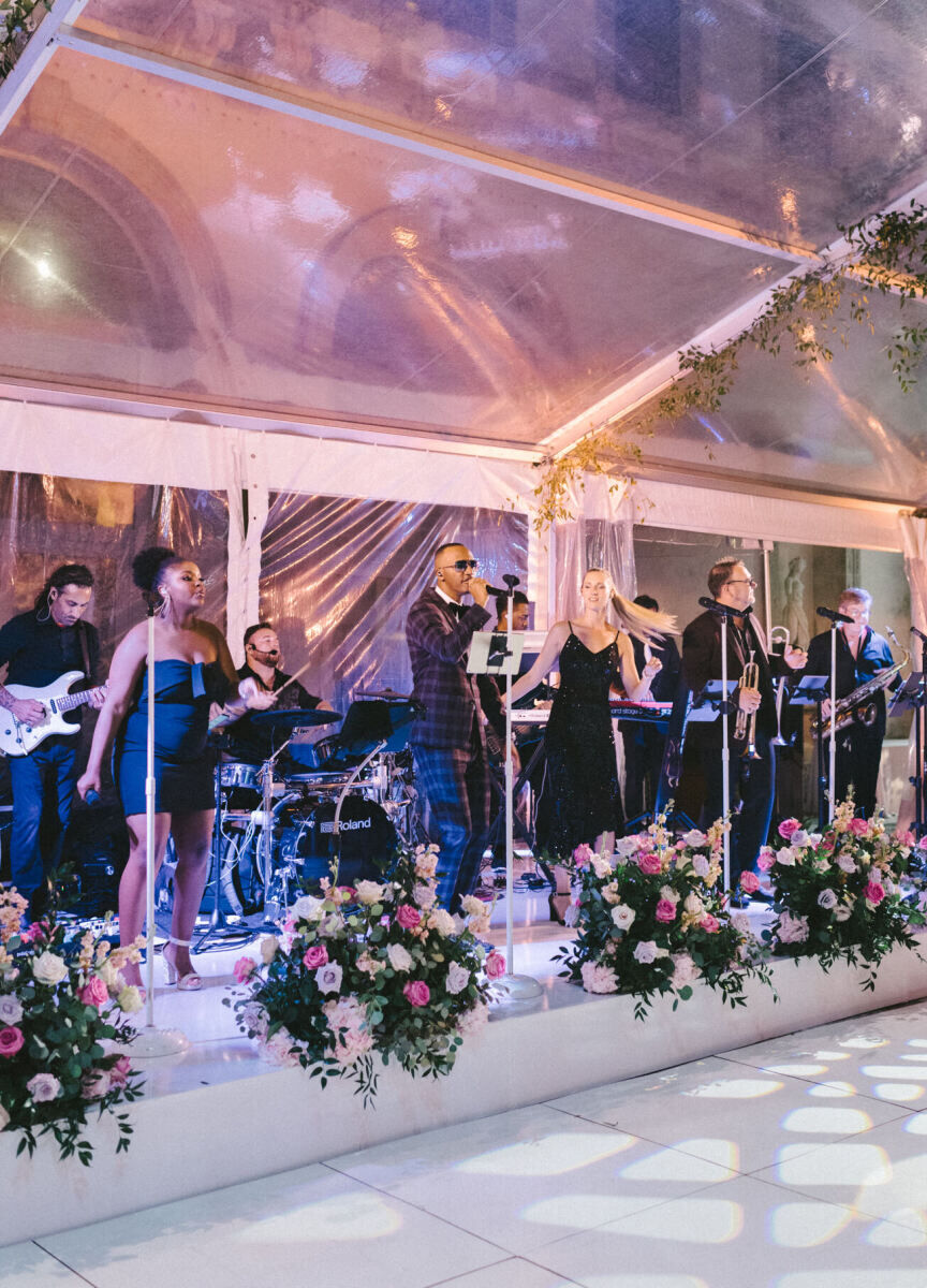 A band plays during a glam, garden wedding reception, in a clear-top tent.