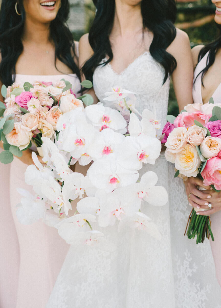 A bride holds a bouquet of white orchids, while bridesmaids hold roses and peonies befitting the glam, garden wedding theme.