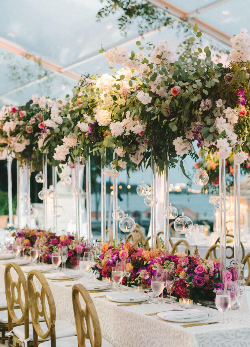 A mix of tall and low arrangements decorate the tables at a glam, garden wedding reception.