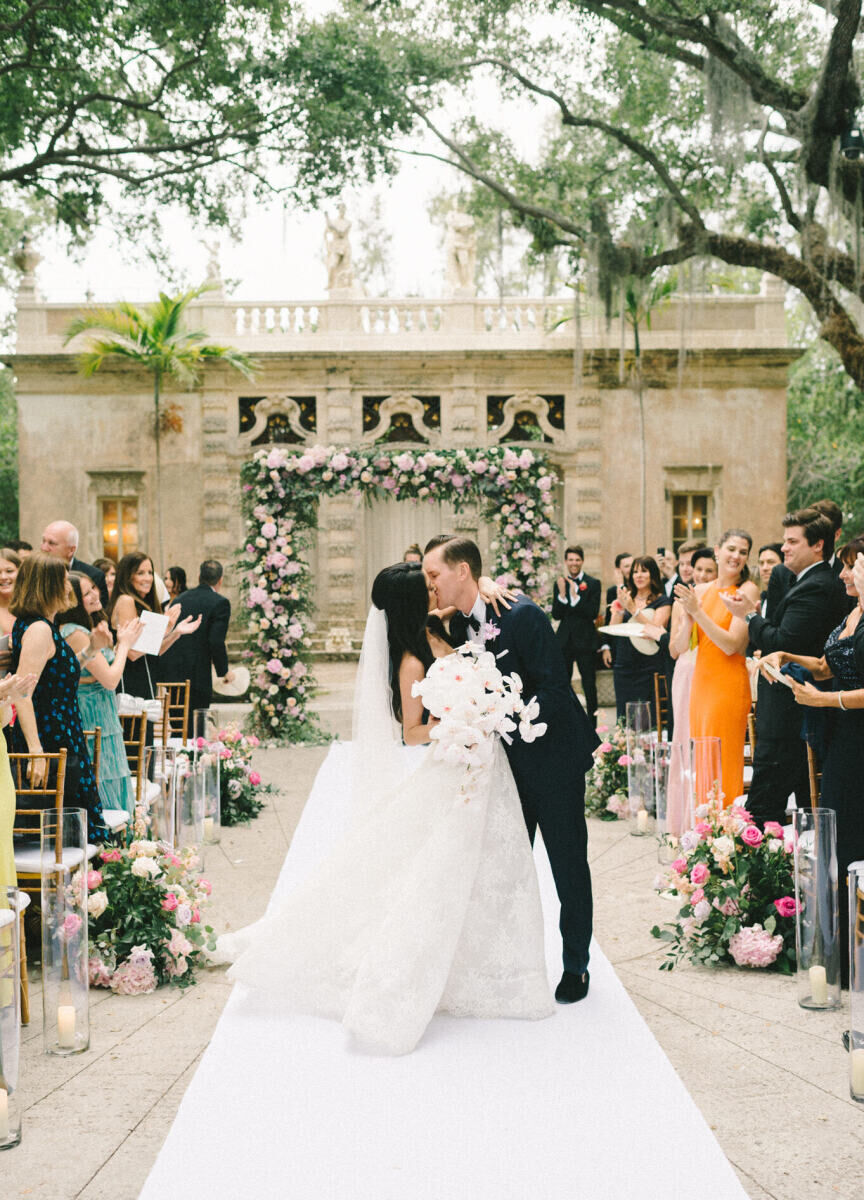 A bride and groom kiss as they walk up the aisle of their glam, garden wedding ceremony.