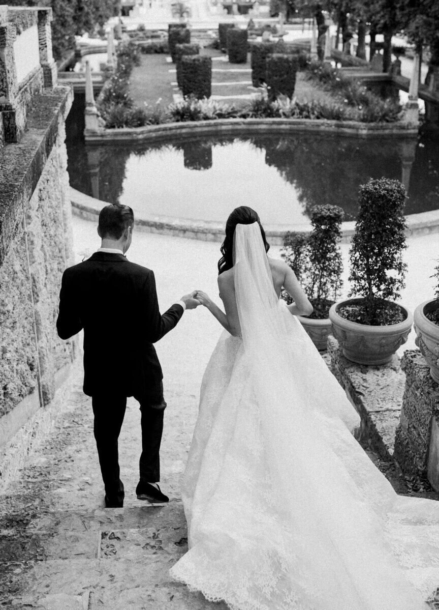 A groom and bride hold hands and walk down the steps during their glam, garden wedding.