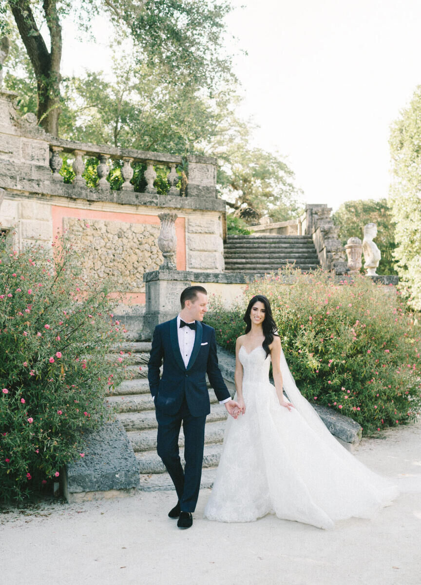 A bride and groom walk the grounds of their wedding venue during their glam, garden wedding.