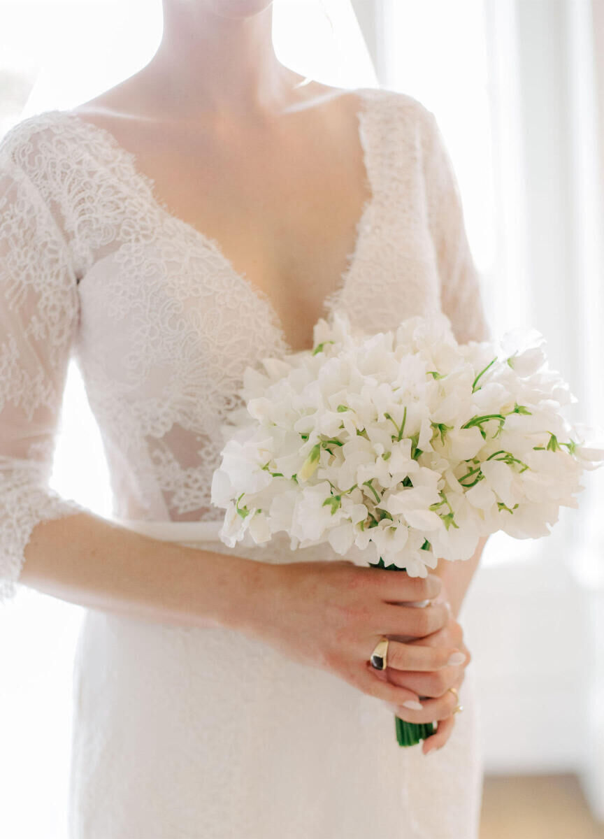 A bride holds her bouquet of white sweet peas before her Glenmere Mansion wedding ceremony.