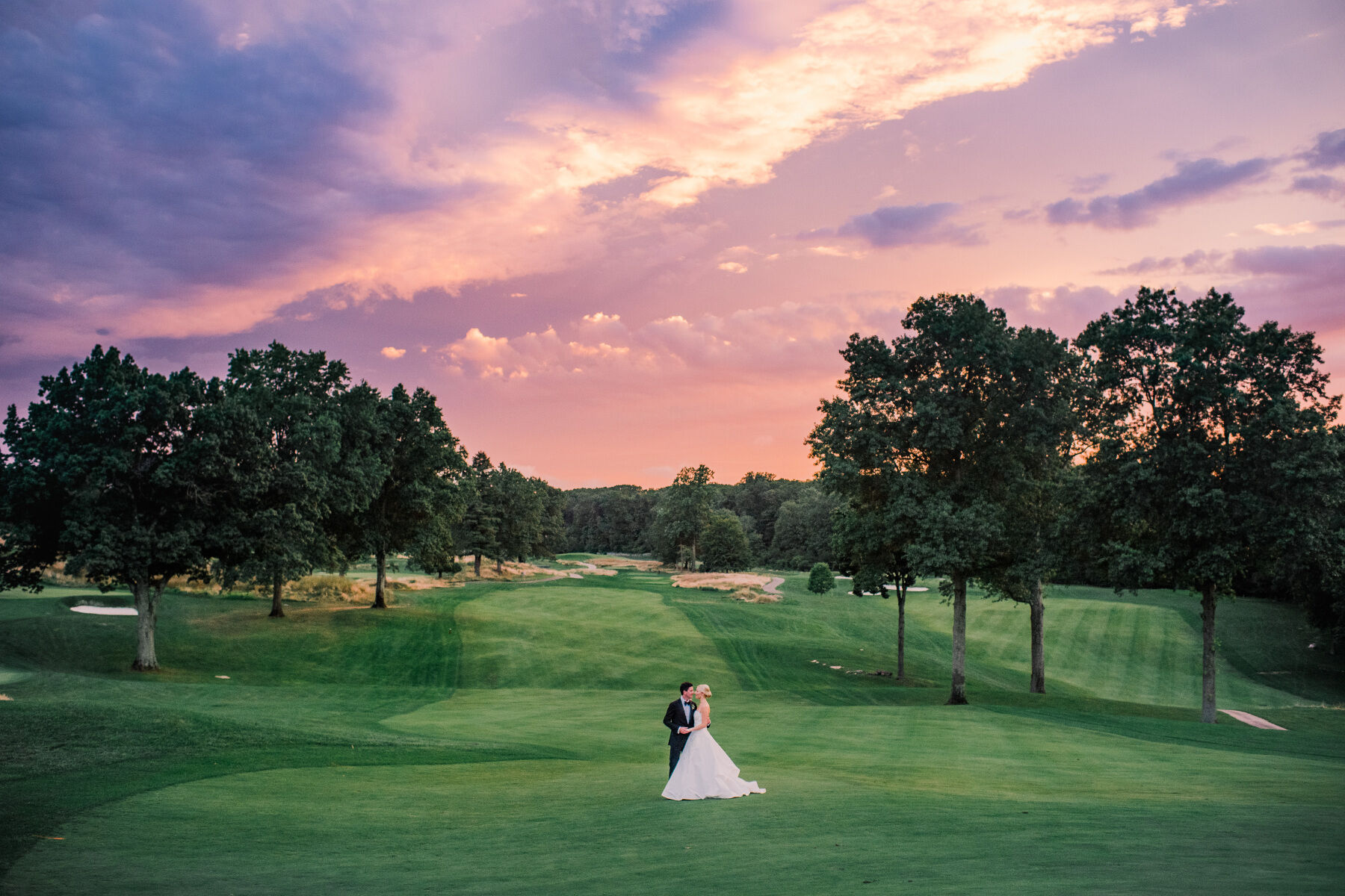 Golf Course Wedding Venues: A wedding couple staring at each other on a golf course with a dramatic sunset in the background.