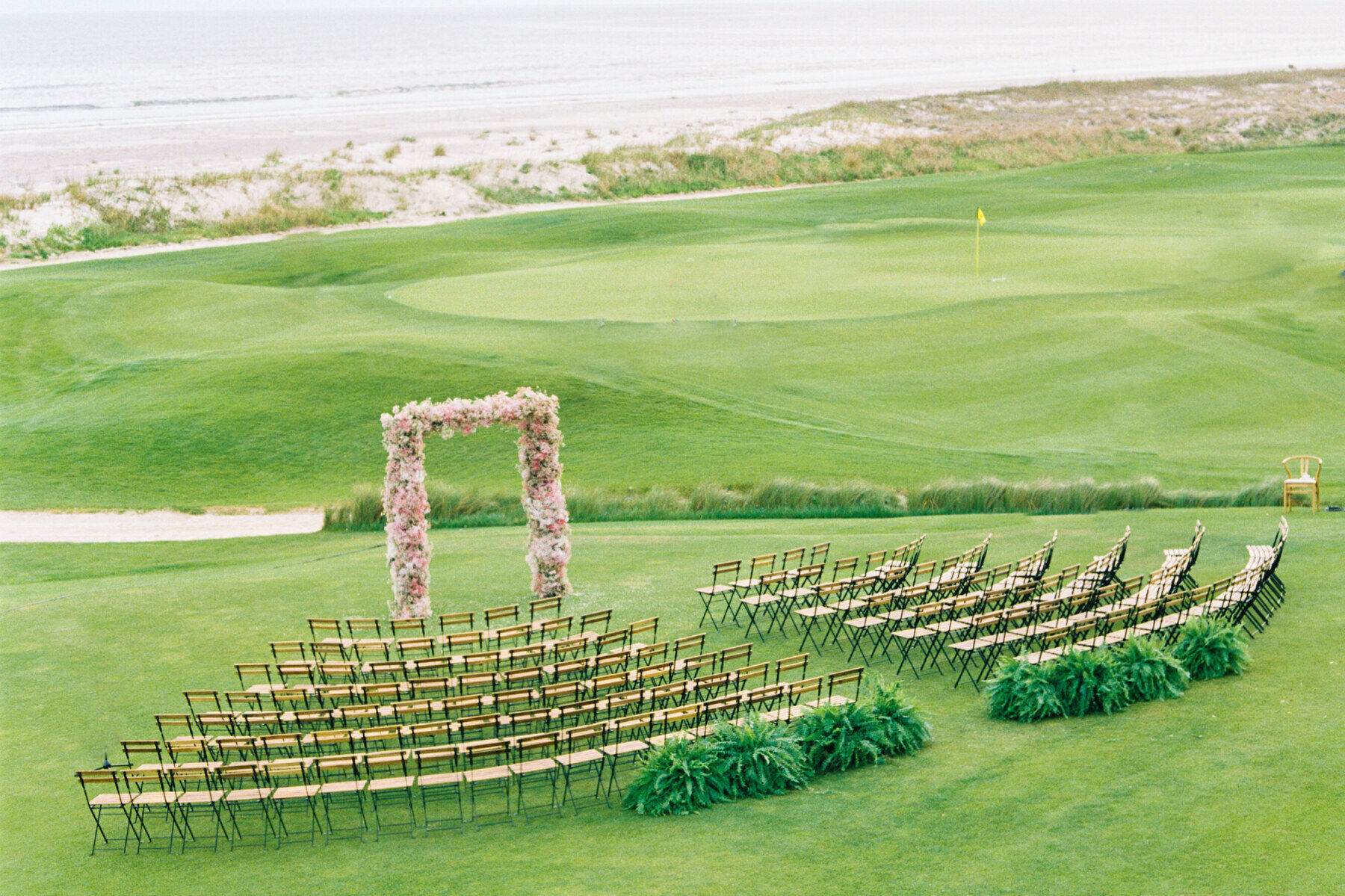 Golf Course Wedding Venues: A wedding ceremony setup with a floral arch and amphitheater-style chairs on a golf course.
