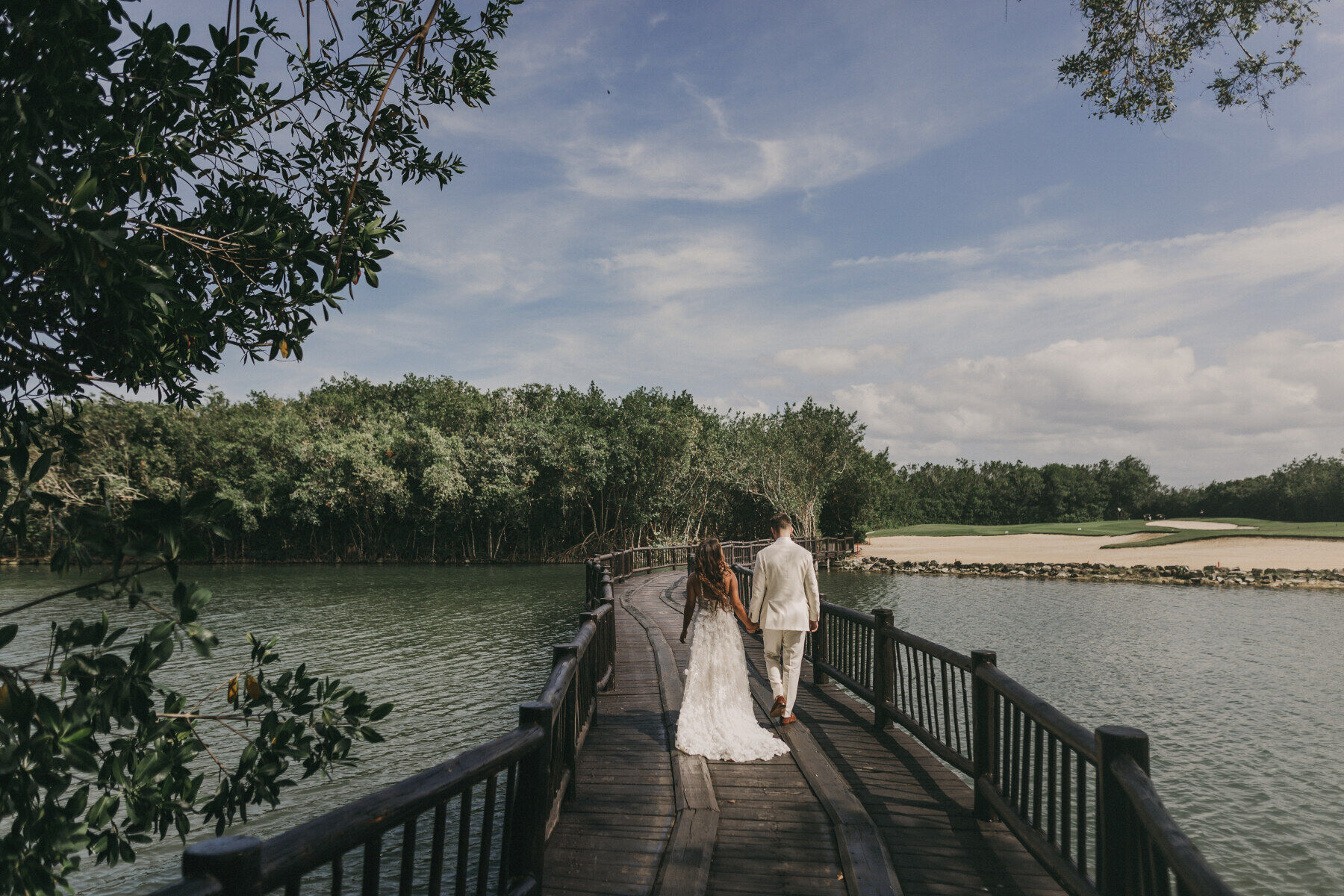 Golf Course Wedding Venues: A wedding couple holding hands while walking over a bridge.