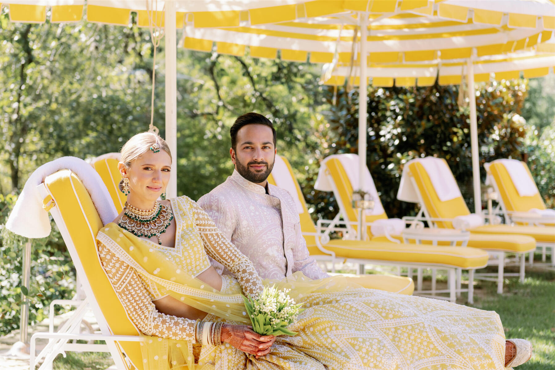 A bride and groom pose for a portrait on yellow lounge chairs at Commodore Perry Estate ahead of their Indian fusion wedding ceremony.