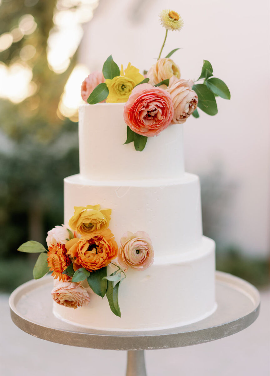 A three-tier wedding cake covered in fresh flowers at an Indian fusion wedding.