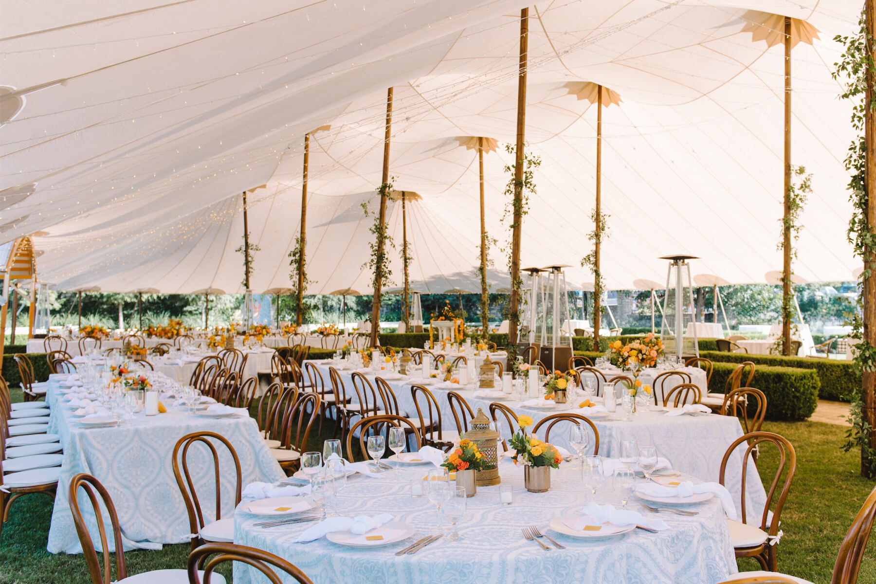 A tented reception at an Indian fusion wedding featured blue-and-white table linens, citrus-hued centerpieces, and poles wrapped with greenery.