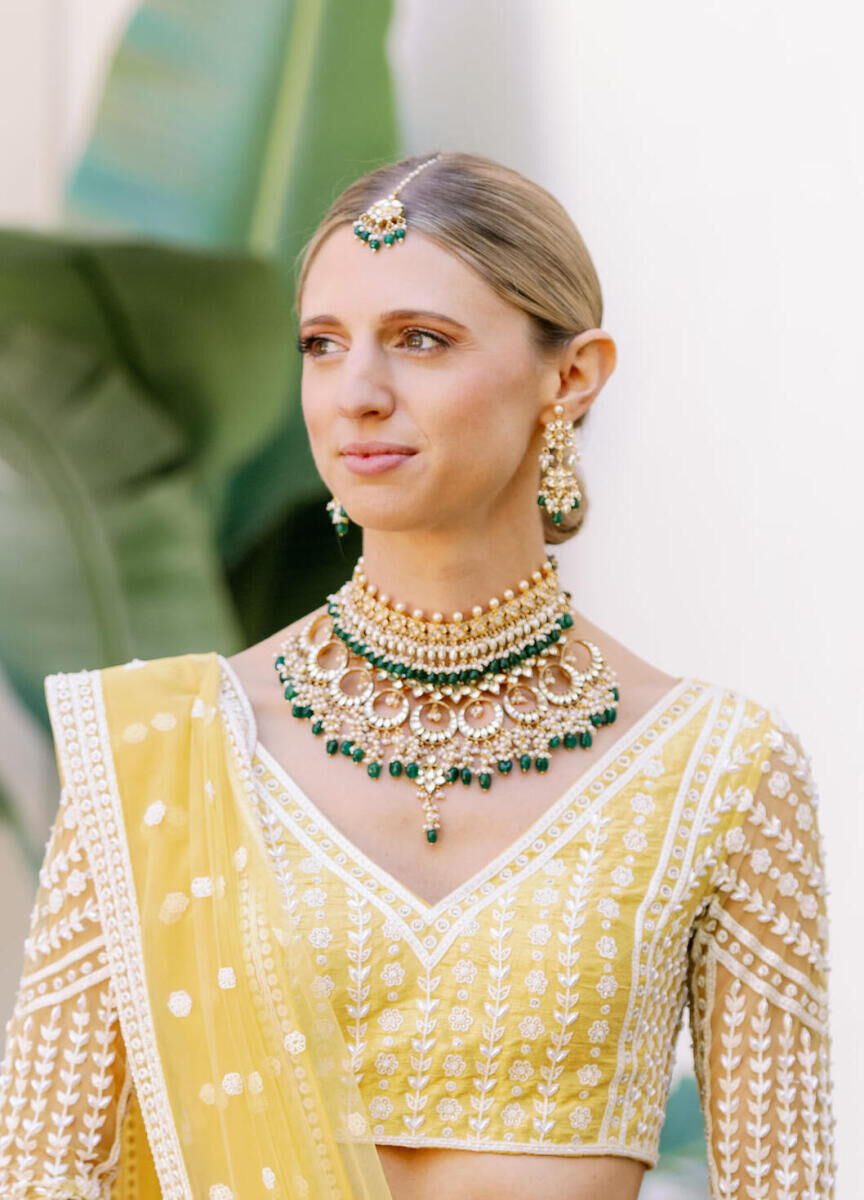 A bride wearing a yellow lehenga and traditional Indian jewelry sported a low-bun for her Indian fusion wedding.