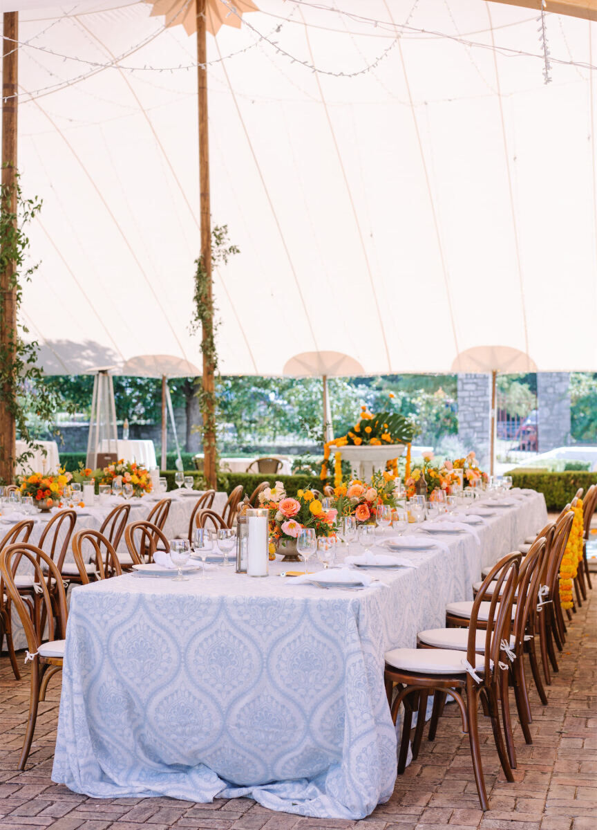 A long table covered in a patterned blue-and-white linen and citrus-colored floral arrangements awaited guests at an Indian fusion wedding reception.
