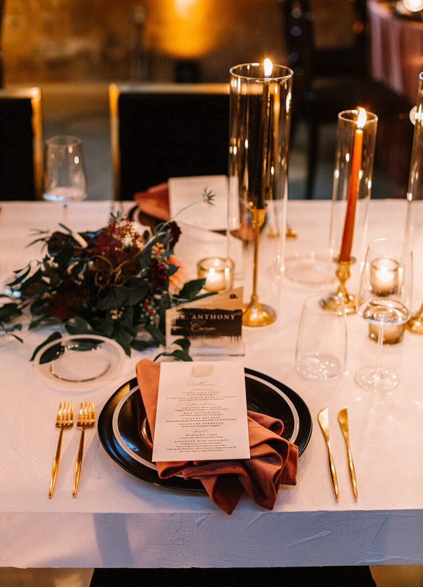 At some tables at this industrial wedding reception, minimal gold flatware, black and white plates, and a rust-colored napkins comprised the place settings.