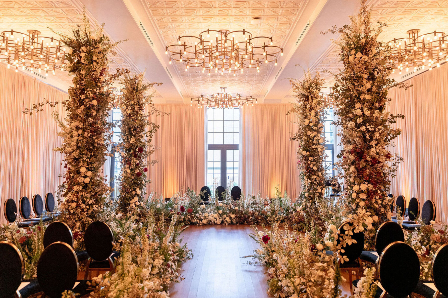 An indoor ceremony in the-the-round with floral columns and black-and-gold chairs.