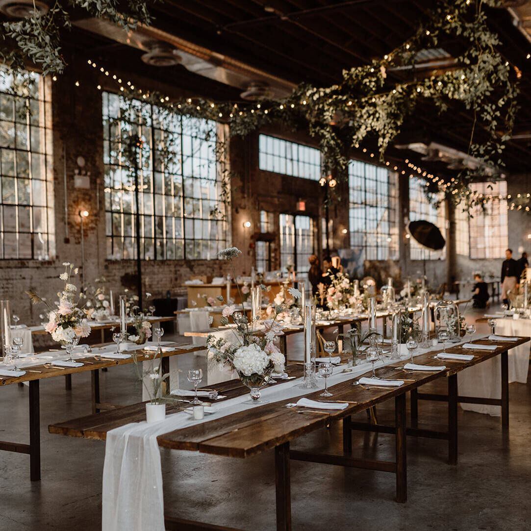 An industrial wedding venue (99 Scott) set up for a reception, with big windows, twinkle lights, long tables, and brick walls.