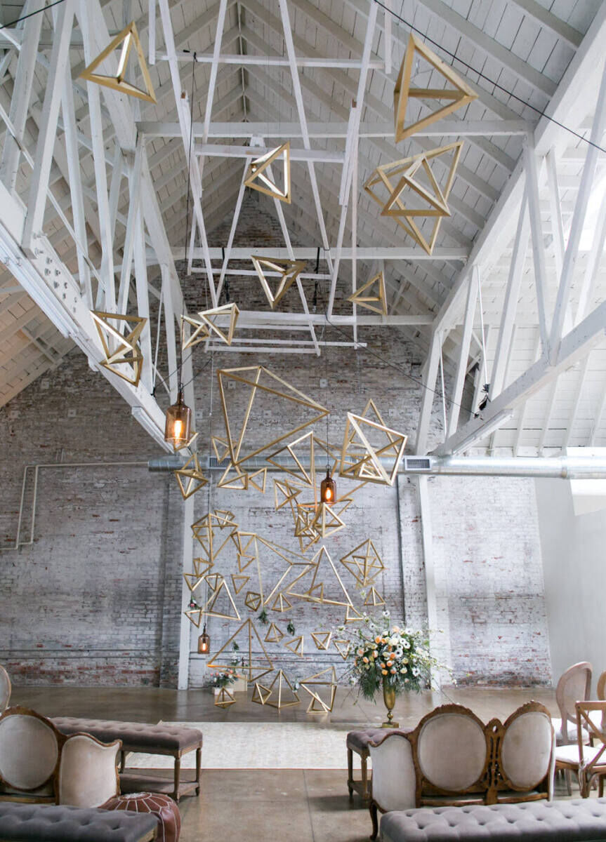 A chic reception set-up with gold geometric shapes hanging from a vaulted ceiling.