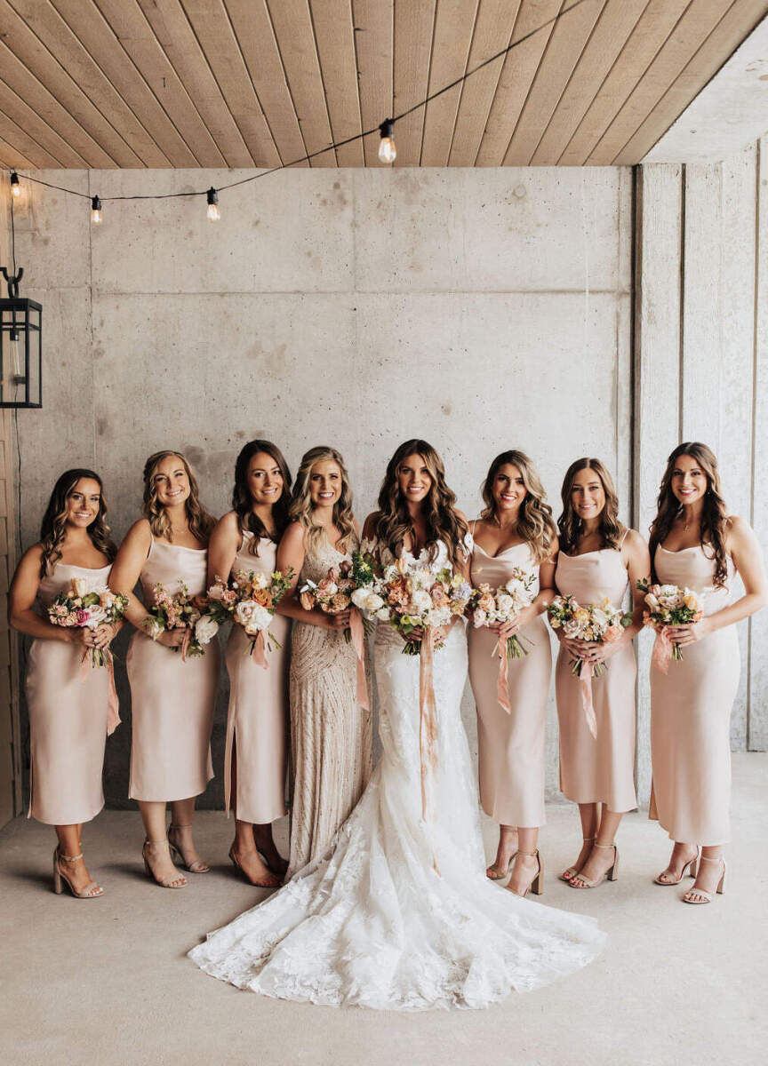 Industrial Wedding Venues: A bride posing for a photo with seven of her bridesmaids against a concrete-inspired wall.