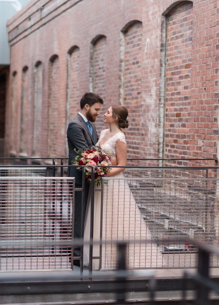 Industrial Wedding Venues: A bride and groom embracing on a metal pathway with lots of brick detailing behind them.