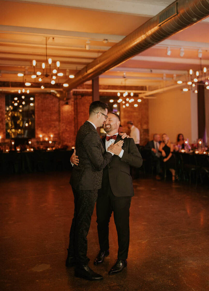 Industrial Wedding Venues: Two grooms slow-dancing together on the dance floor of Senate Garage.