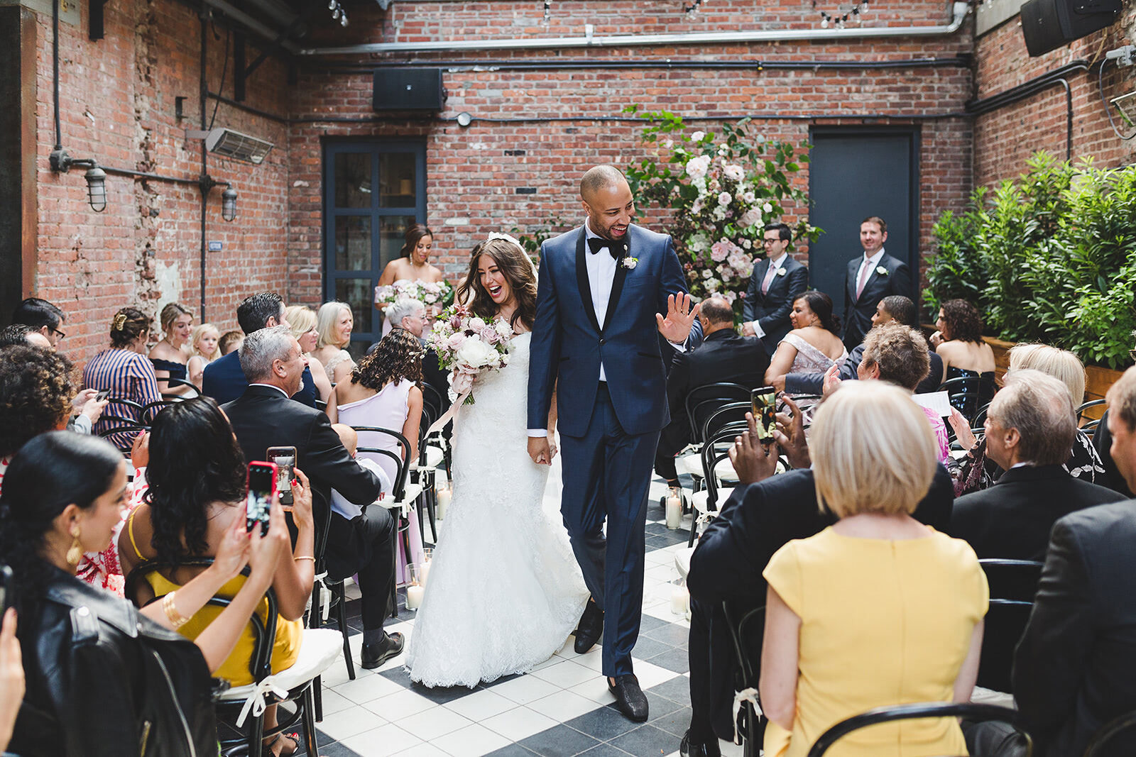 Industrial Wedding Venues: A bride and groom smiling, holding hands, and walking back down a narrow aisle together at Wythe Hotel.