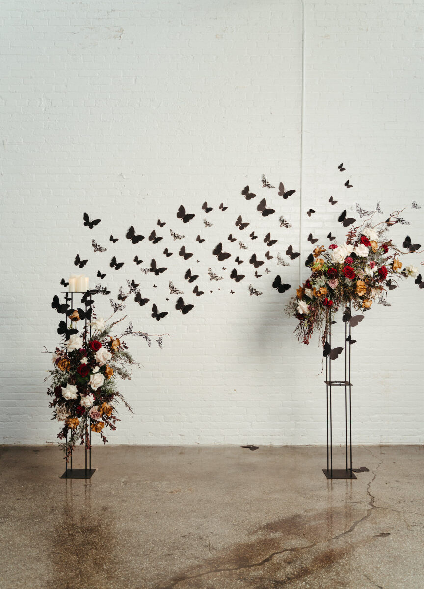 Industrial Wedding Venues: A minimalistic floral ceremony set-up with black butterflies on a white-brick wall with concrete flooring.