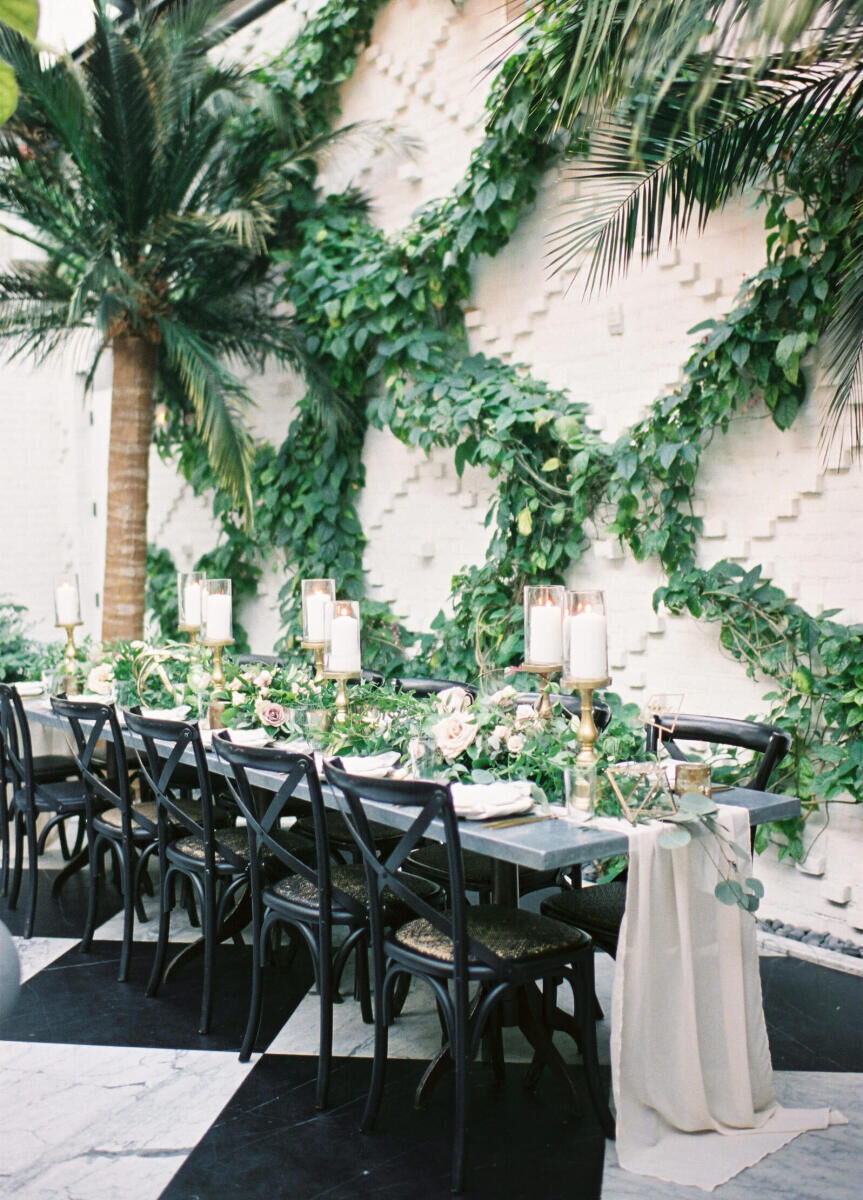 Industrial Wedding Venues: A black reception table and chairs in front of an intricate white wall with greenery sprawled across it.