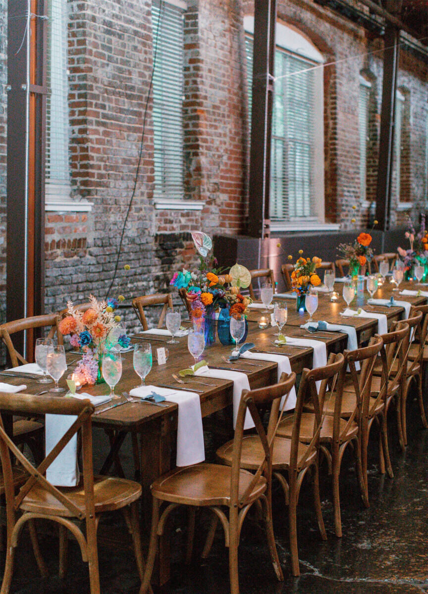 Industrial Wedding Venues: A reception table set-up with colorful flowers against a brick wall.