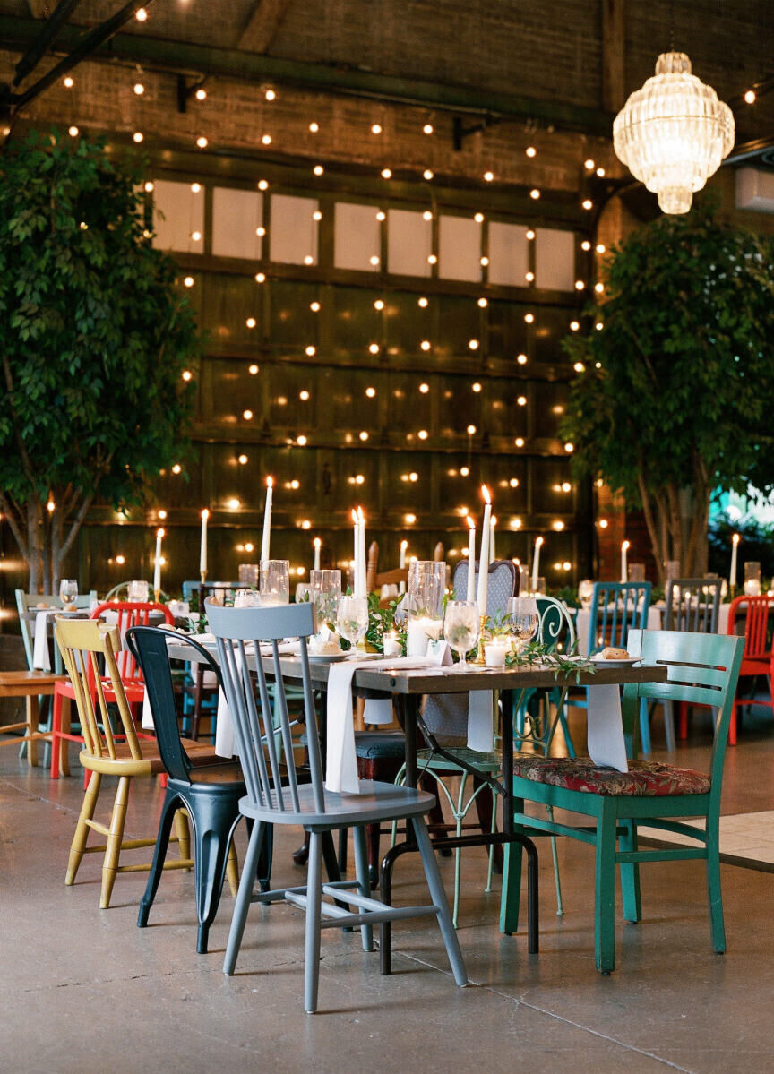 Industrial Wedding Venues: A reception set-up with cool mismatched chairs and a table in front of a garage-style door lined with string lights.